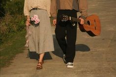 a man and woman are walking down the street with guitars in their hands while holding flowers