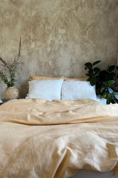 an unmade bed with two pillows and some plants on the nightstands next to it