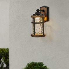 a wall mounted light on the side of a white building with trees in the background