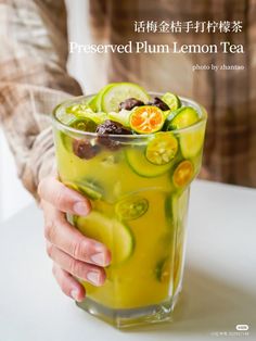 a person holding a glass filled with liquid and cucumber slices on top of it