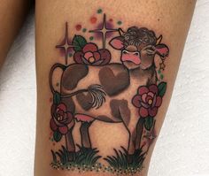 a tattoo with a cow and flowers on it's leg, next to a cross