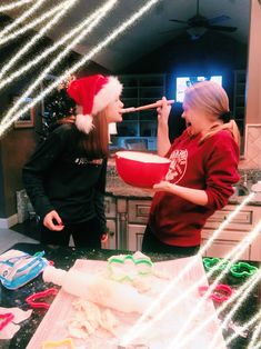 two girls in the kitchen with christmas decorations on the counter and one girl is holding a spoon