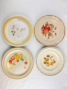 four plates with floral designs on them sitting on a tableclothed surface, all decorated in different colors and sizes