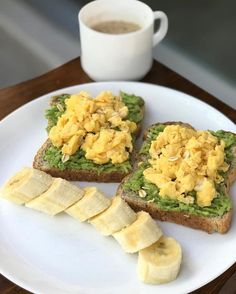 two pieces of toast with avocado and scrambled eggs on them, sitting on a plate next to a cup of coffee