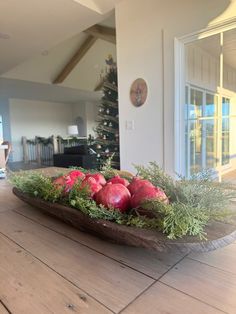 a wooden bowl filled with apples and greenery on top of a wooden table next to a christmas tree