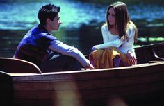 a man and woman sitting in a small boat on the water looking at each other