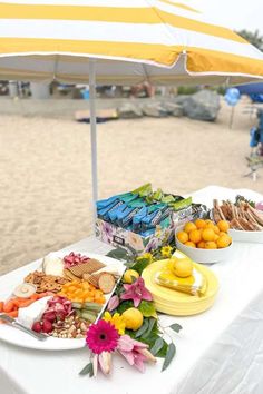 a white table topped with plates of food next to an umbrella on top of a beach