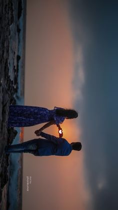 two people standing next to each other on a beach at sunset with the sun behind them