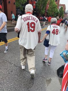 an older couple walking down the street holding hands and wearing baseball jerseys with numbers on them