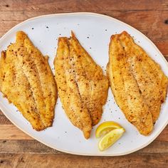 three fish fillets on a white plate with lemon wedges