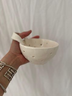 a hand holding a white ceramic bowl with silver rings on it's thumb and wrist