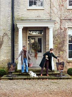 two people and a dog standing in front of a house with their hands out to each other