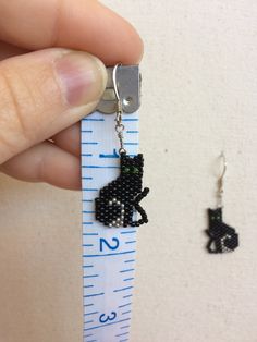 a hand holding a measuring tape with a black cat charm on it's end