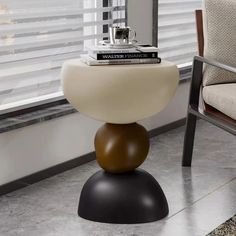 a table with a book on top of it next to a chair in front of a window