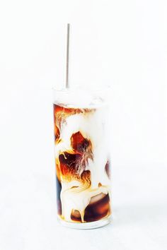 a glass filled with liquid and ice on top of a white table next to a straw