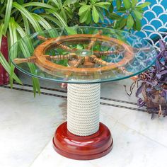 a glass table topped with a wooden boat wheel and rope on top of a white tile floor