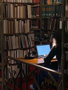 a woman sitting at a table with a laptop in front of a bookshelf