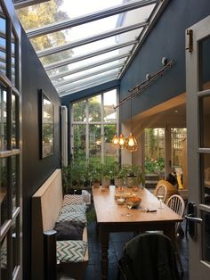 an indoor dining area with wooden table and chairs under a glass roof over looking the garden