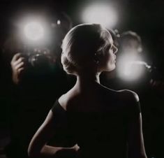 a woman standing in front of a group of people with lights on her head and hands behind her back