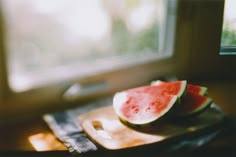 a slice of watermelon sitting on top of a cutting board next to a window