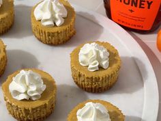 several cupcakes on a white plate with whipped cream and honey in the background