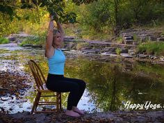 a woman is sitting on a chair in front of a river and stretching her arms