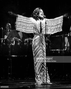 an image of a woman singing on stage with her arms spread out and hands outstretched