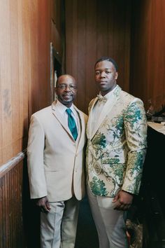 two men in suits standing next to each other near a wall with wood paneling