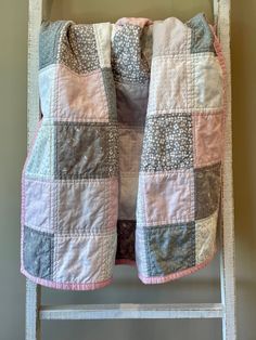 a pink and gray patchwork jacket hanging on a ladder next to a white wall