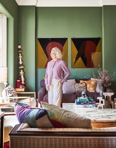 a woman standing in the middle of a living room with green walls and paintings on the wall