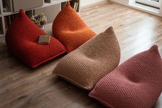 three different colored pillows on the floor in front of a bookcase with bookshelves