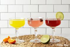 three different colored drinks sitting on top of a wicker tray next to an orange slice