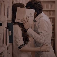 a man and woman kissing in front of a bookcase with books on the shelves