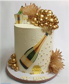 a white cake decorated with gold decorations and a bottle of champagne on the top tier