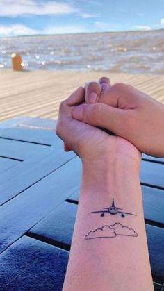 two hands holding each other with an airplane tattoo on their wrist and the ocean in the background