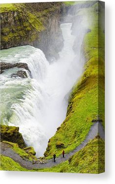 two people are standing at the edge of a cliff overlooking a large waterfall with water pouring over it