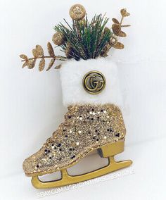 a pair of gold and white ice skates decorated with glitter, pine needles and a gg brooch