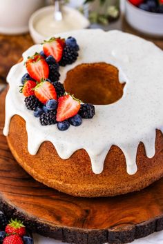 a bundt cake with white icing and berries on top, sitting on a wooden platter