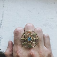 "What a knockout! This textured raw brass gold tone ring is set with the Earth in glass surrounded by 8 different phases of the moon in a round halo. Celebrate the cosmos and our planetary home with this piece of galaxy jewelry! Ring Size: Adjustable Design Size: 1 1/4\" (3.2cm) Materials: Raw brass, glass ★ These are individually handcrafted and the particular piece you receive may vary slightly from what is pictured. These are also not 100% waterproof, so please avoid submerging them in water. Nickel-free Celestial Moon Ring, Spiritual Gold Moon-shaped Ring, Spiritual Gold Moon Shaped Ring, Spiritual Moon Shaped Gold Ring, Celestial Adjustable Midi Rings, Celestial Metal Ring Jewelry, Celestial Style Metal Ring Jewelry, Symbolic Gold Rings With Sun And Moon Design, Celestial Style Gold Round Rings