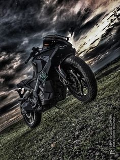 a black motorcycle parked on top of a lush green field under a cloudy blue sky