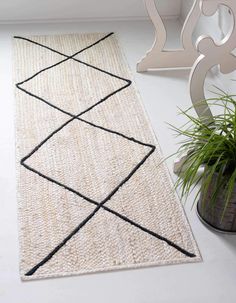 a white rug with black lines on it next to a chair and potted plant