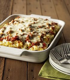 a casserole dish with meat and cheese in it on a wooden table next to silverware