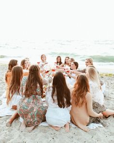 a group of young women sitting on top of a sandy beach next to the ocean