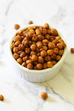 a white bowl filled with chickpeas on top of a marble counter next to nuts