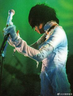 a man holding a microphone in his right hand while standing on stage with green lights behind him