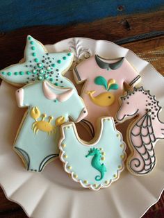 some decorated cookies on a white plate with blue and pink icing in the shape of seahorses