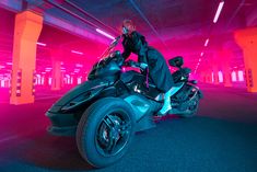 a man riding on the back of a black motorcycle in a parking garage with neon lights