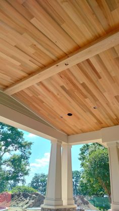 an outdoor covered patio area with columns and wood ceilinging on the side of it