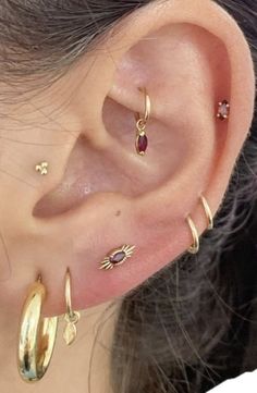 a woman wearing gold ear piercings with red stones on her left ear and two small hoop