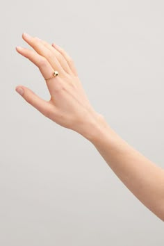 a woman's hand with a gold ring on her left wrist, against a gray background